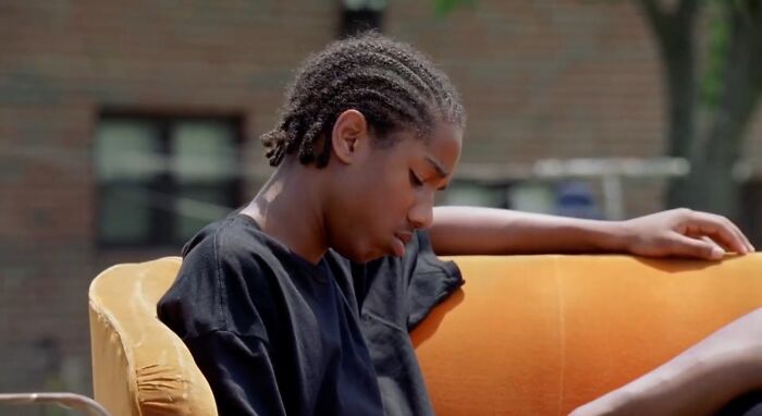 Young person sitting on an orange couch outdoors, looking down with a solemn expression, depicting tragic losses in TV shows.
