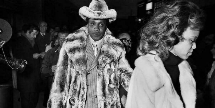 Man in a fur coat and hat walking confidently among a crowd, showcasing fascinating and interesting fashion moments.