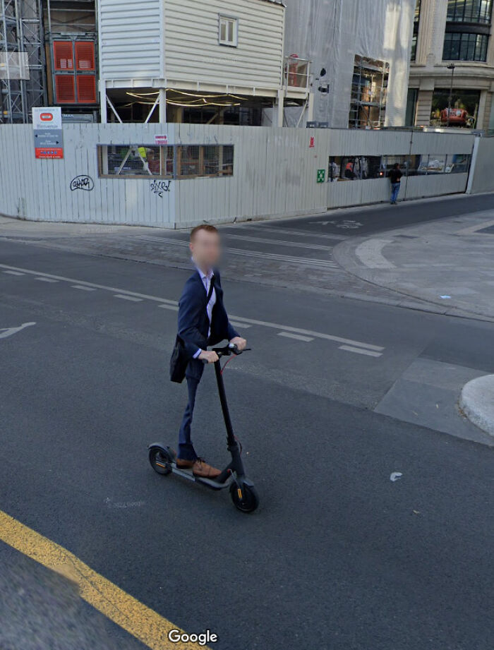 Man in business attire riding an electric scooter on street captured in funny Google Maps shenanigans.