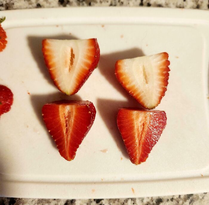 Close-up comparison of four strawberry halves showing variety in color and texture on a white cutting board.