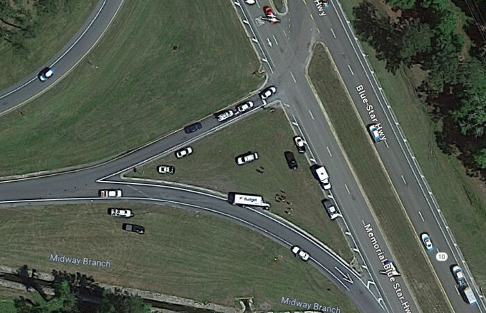 Aerial view of a traffic incident with multiple vehicles stopped on a grassy highway median captured on Google Maps.