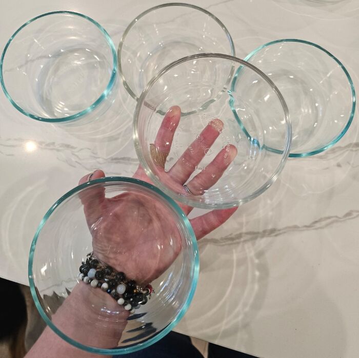Hand holding clear glass bowls of different sizes arranged on a marble surface in a fascinating comparison pic.