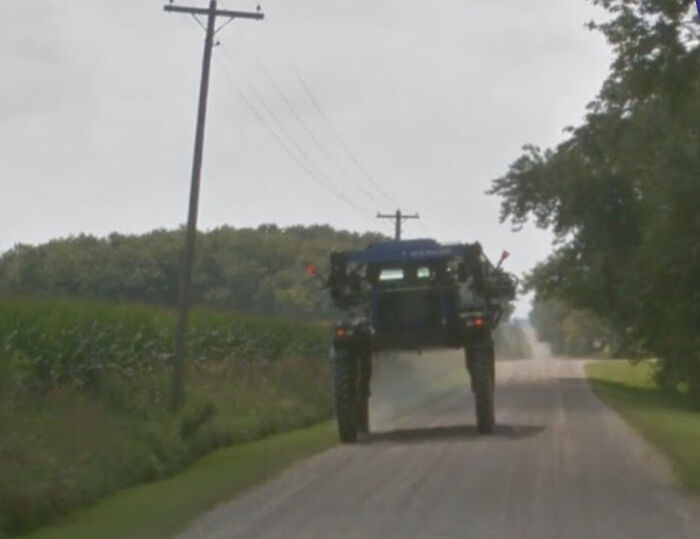 Large farm vehicle driving down a rural road captured on Google Maps showing unusual shenanigans in a countryside setting.