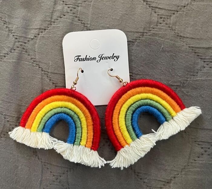 Rainbow pride earrings made of colorful thread with white fringes, displayed on a fashion jewelry card against a gray background.