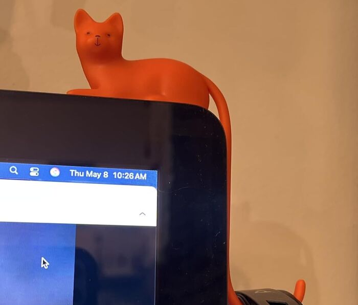 Orange cat-shaped desk accessory perched on a computer monitor, one of the desk items to make 9-to-5 less blah.