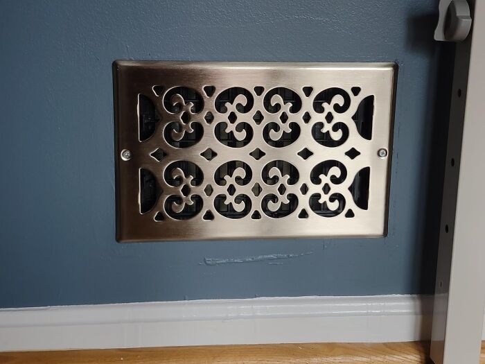 Decorative metal vent cover installed on blue wall hiding an ugly eyesore in home interior design.