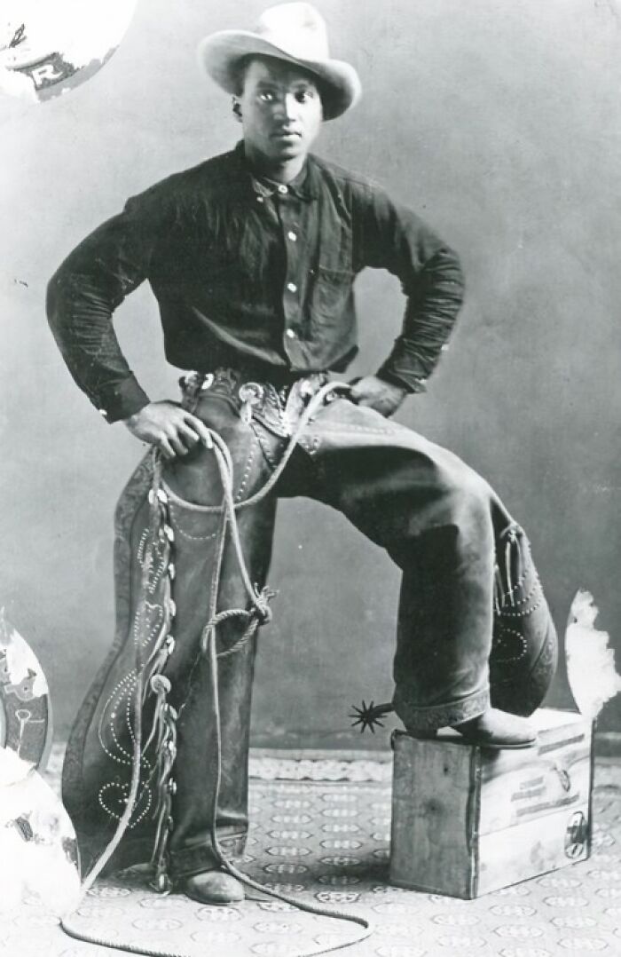 Vintage cowboy dressed in traditional gear with hat and chaps posing confidently holding a lasso in an old photograph.