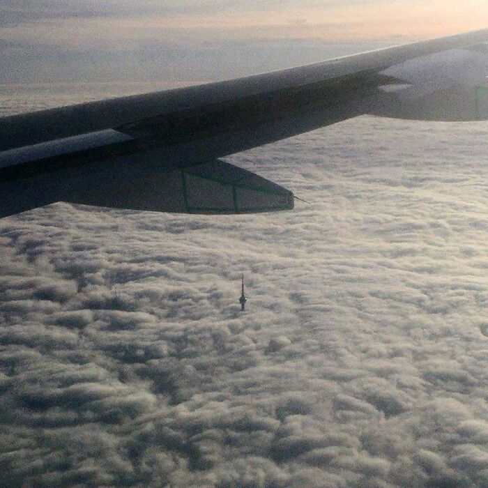 A famous landmark peak rising above dense clouds captured from an airplane wing, showing an unexpected angle.