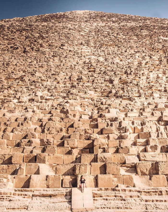 View of famous landmarks from unexpected angles showing the pyramid's massive stone blocks with a person sitting at the base