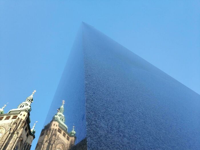 Famous landmarks reflected on a triangular polished stone surface captured from an unexpected angle against a clear blue sky.