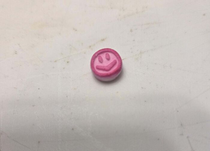 Small pink mystery object with a smiley face design resting on a worn white surface, part of online group recognition.
