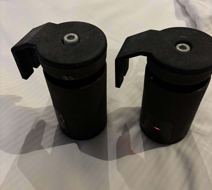 Two black mystery objects with circular tops and side hooks placed on a white surface from an online group recognition post.