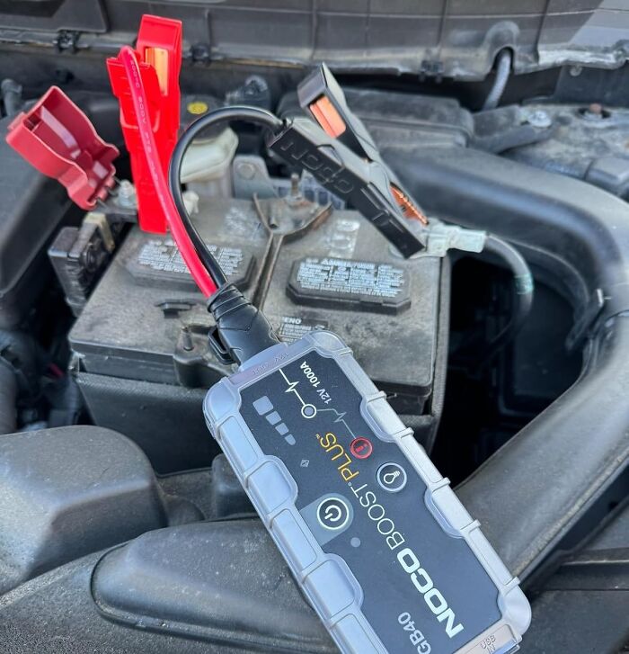 Portable NOCO Boost Plus device connected to a car battery for quick and safe jump-starting.