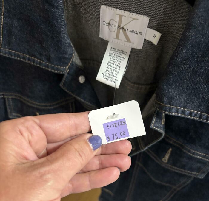 Hand holding a $75 price tag on a Calvin Klein denim jacket found at a thrift store, a ridiculous thrift store find.