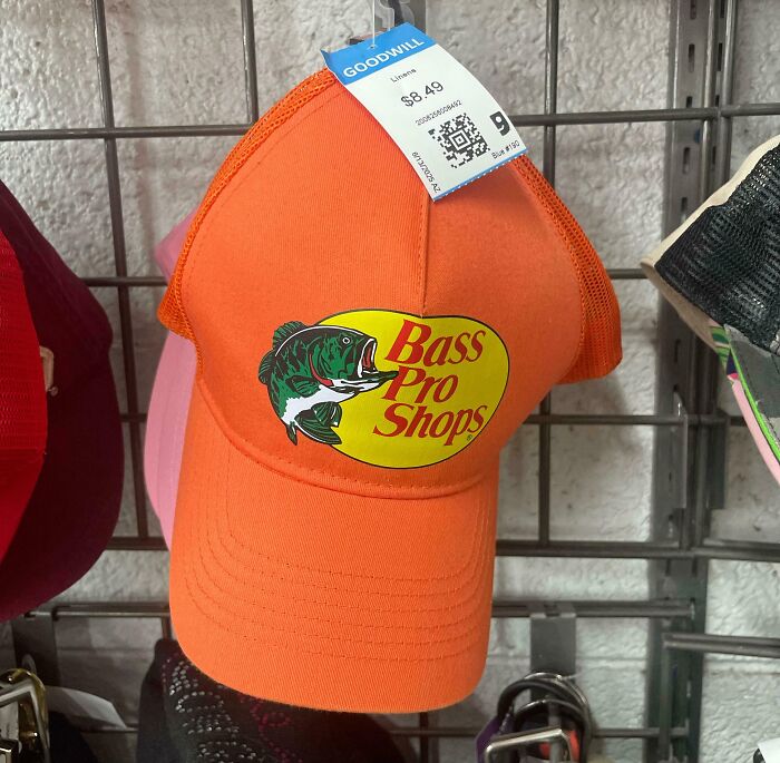 Orange Bass Pro Shops hat with Goodwill thrift store price tag hanging on display rack at thrift store.