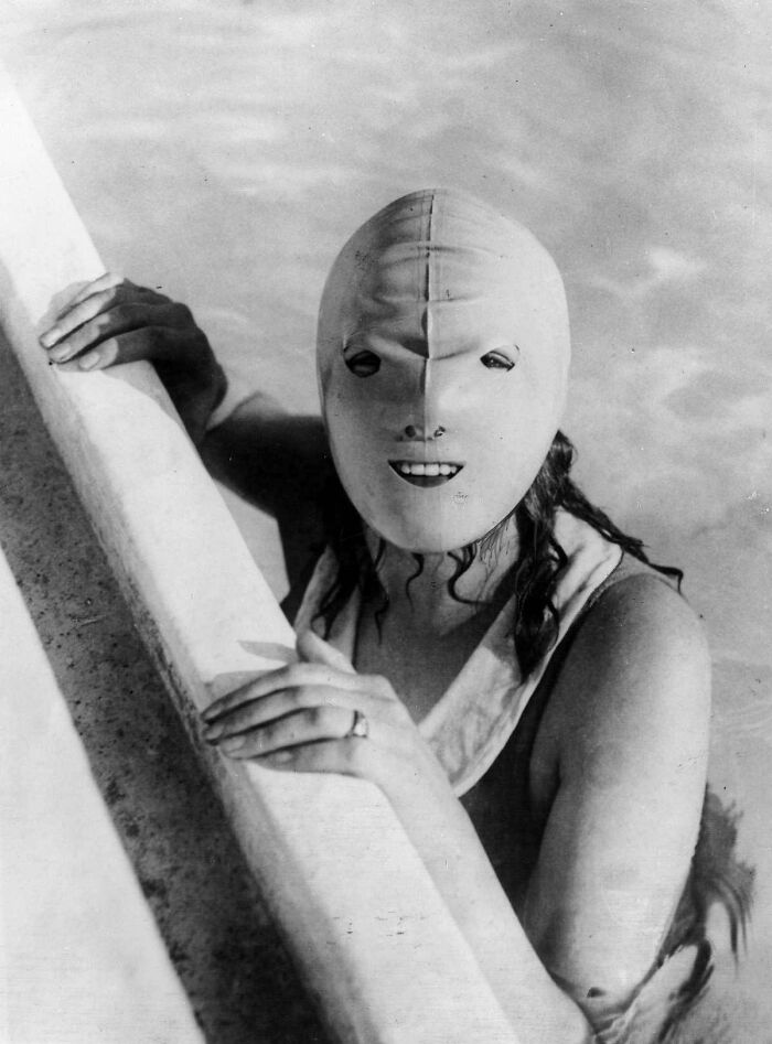 Person wearing a creepy old-fashioned swim mask while holding onto the edge of a pool in an unsettling photo from the past.