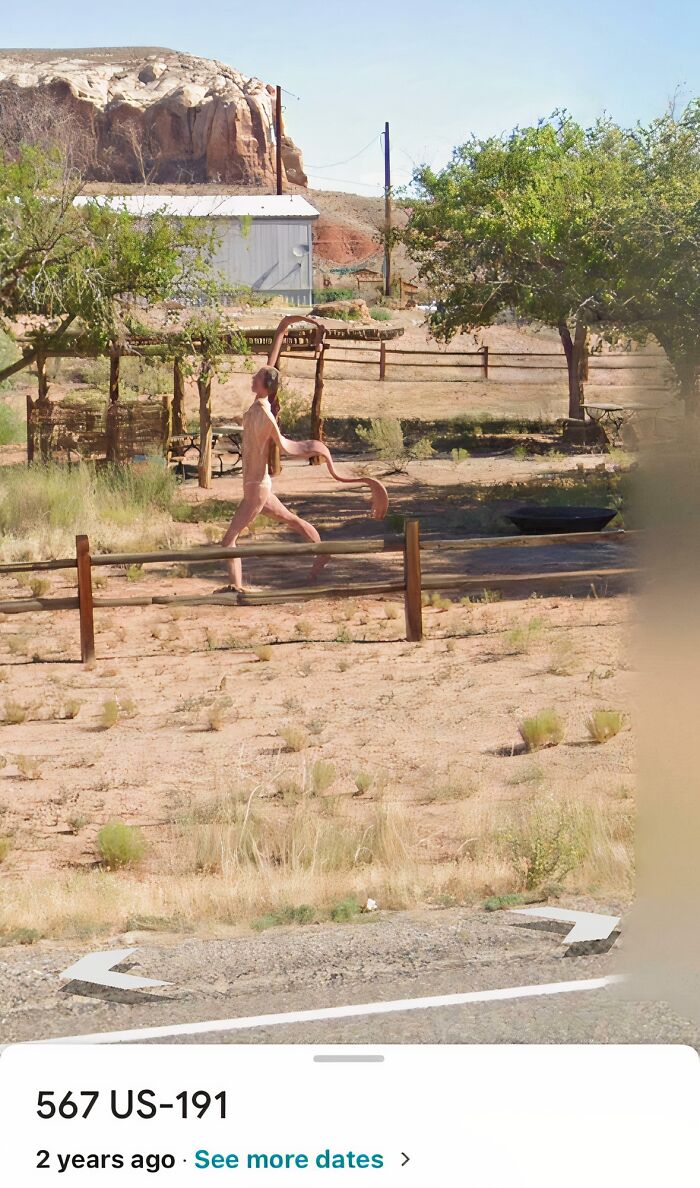 Sculpture of a walking humanoid figure with an extended arm in a dry, desert-like area captured on Google Maps.