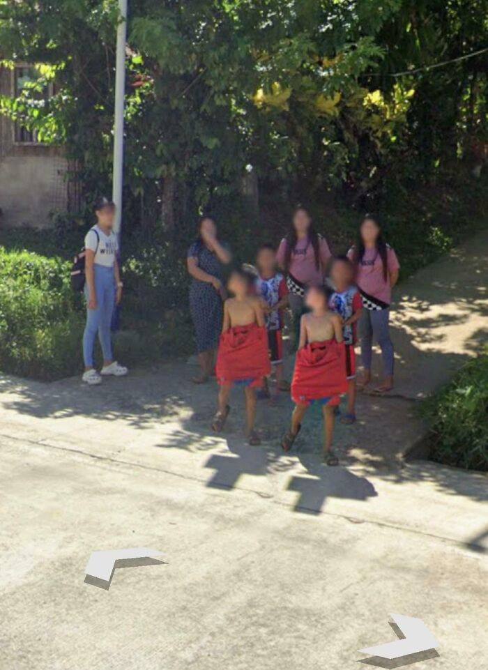 Group of people including children and adults caught in unusual moment on a street, captured in Google Maps shenanigans.