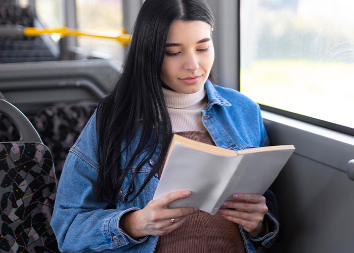 Young woman reading a book while sitting on public transport, capturing a quiet moment amid the humorous and bizarre rides.