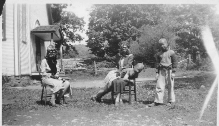 Black and white vintage photo showing children wearing creepy masks and dolls in an unsettling outdoor scene.