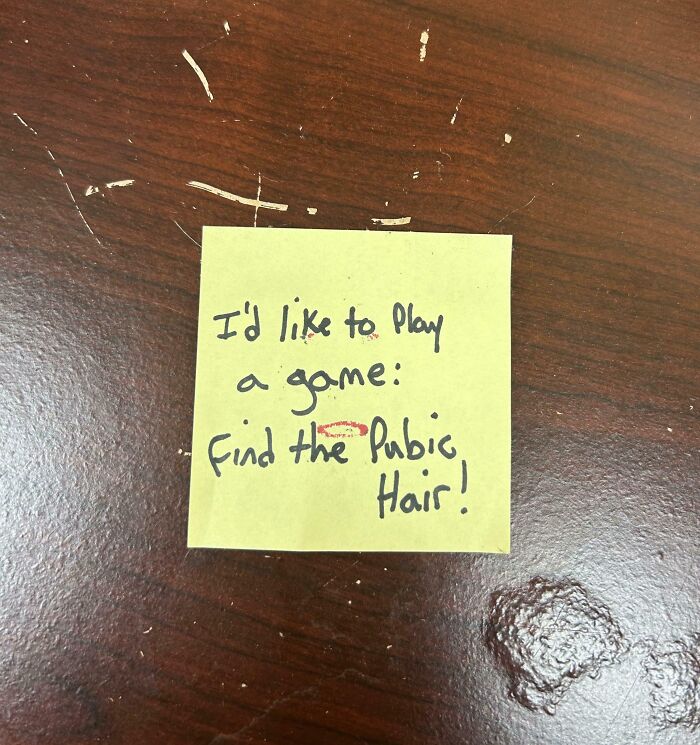 Sticky note on scratched desk in toxic work environment referencing finding pubic hair game.
