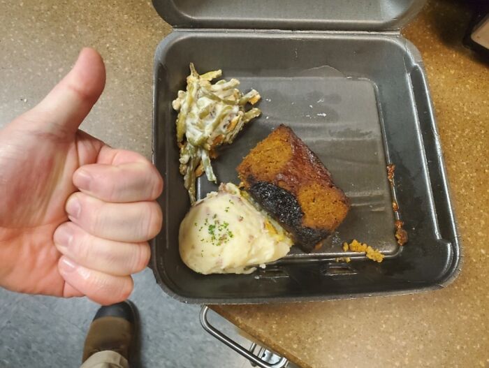 Partially eaten burnt work lunch in a black container with a hand giving a thumbs-up in an extremely toxic work environment.