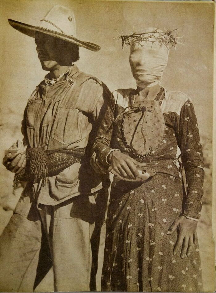 Sepia-toned photo of two people, one wearing a large hat, the other with face bandaged and crowned with barbed wire, creepy vintage image.
