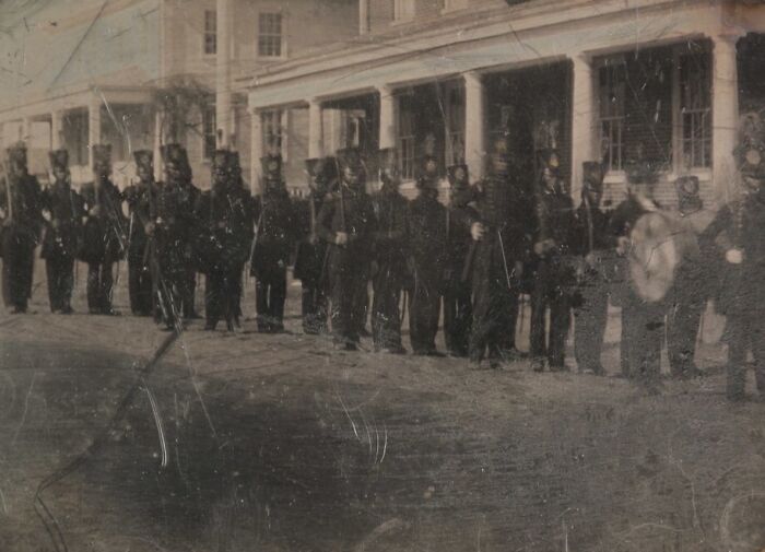 Historic black soldiers standing in formation outside a building, representing African American military history.