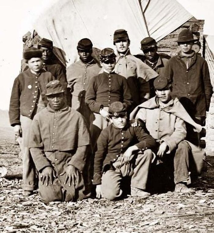 Group of African American soldiers in historical military uniforms posing outdoors during African American military history era.