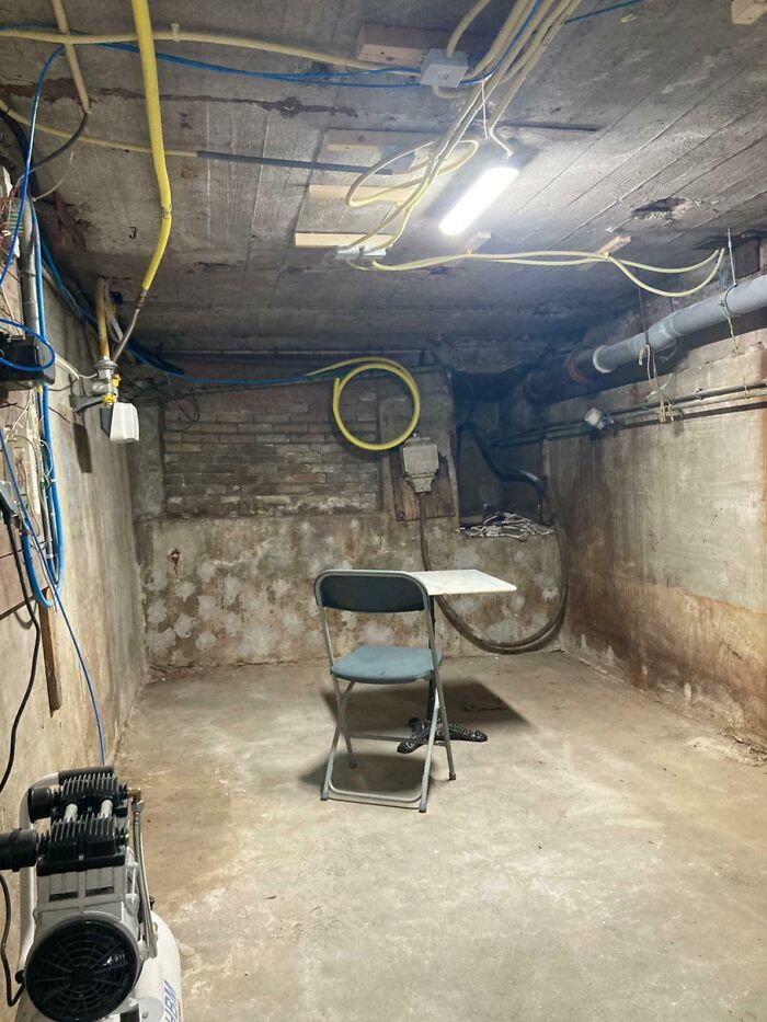 A small, dimly lit, and dirty basement room with exposed pipes and wires, illustrating an extremely toxic work environment.