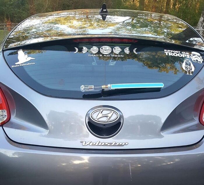 Rear of a silver Hyundai Veloster with clever car finds including themed decals and a lightsaber windshield wiper on the back window.