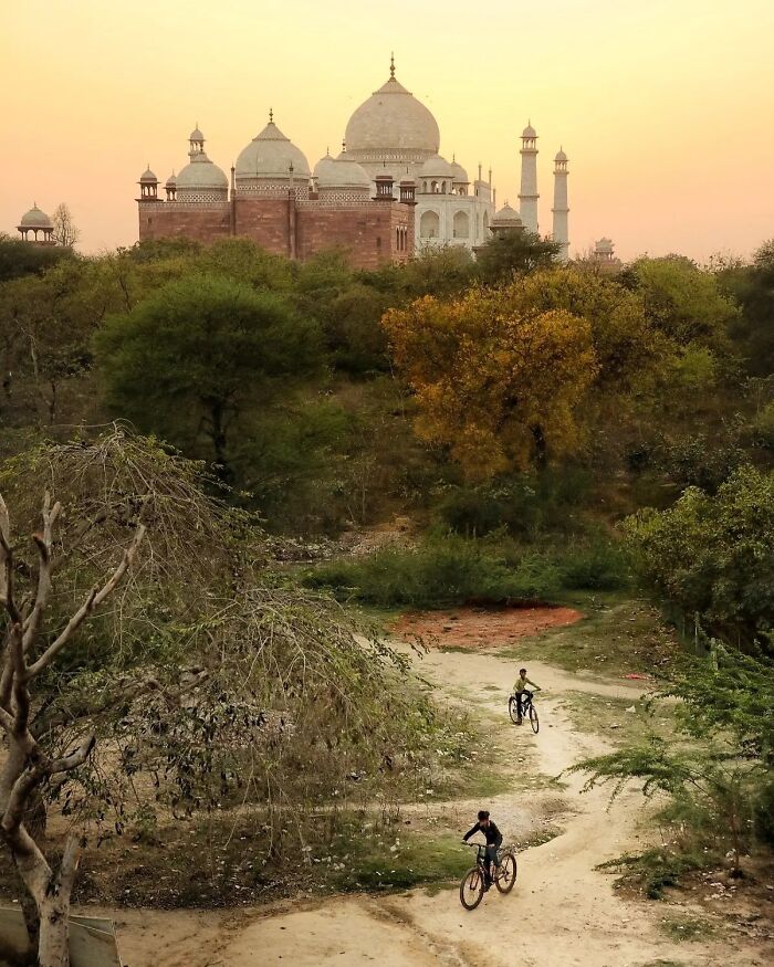 A famous landmark seen from an unexpected angle with cyclists riding on a dirt path surrounded by trees at sunset.