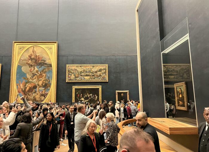 Crowd viewing famous landmarks from unexpected angles inside a museum with large classic paintings and reflections.