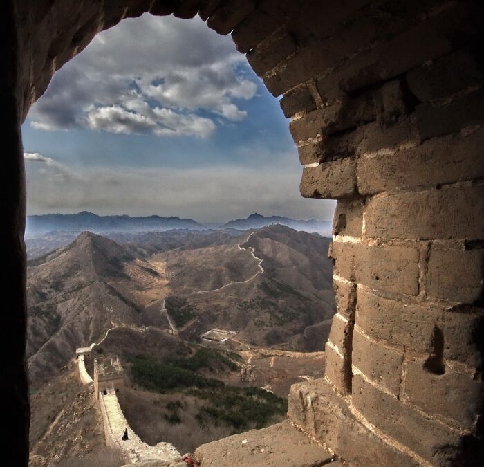 View of the Great Wall of China from an unexpected angle through a stone arch, showcasing famous landmarks and rugged mountains.