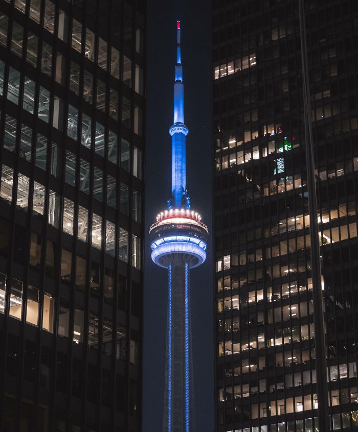 Night view of a famous landmark showing an unexpected angle framed by two illuminated skyscrapers.