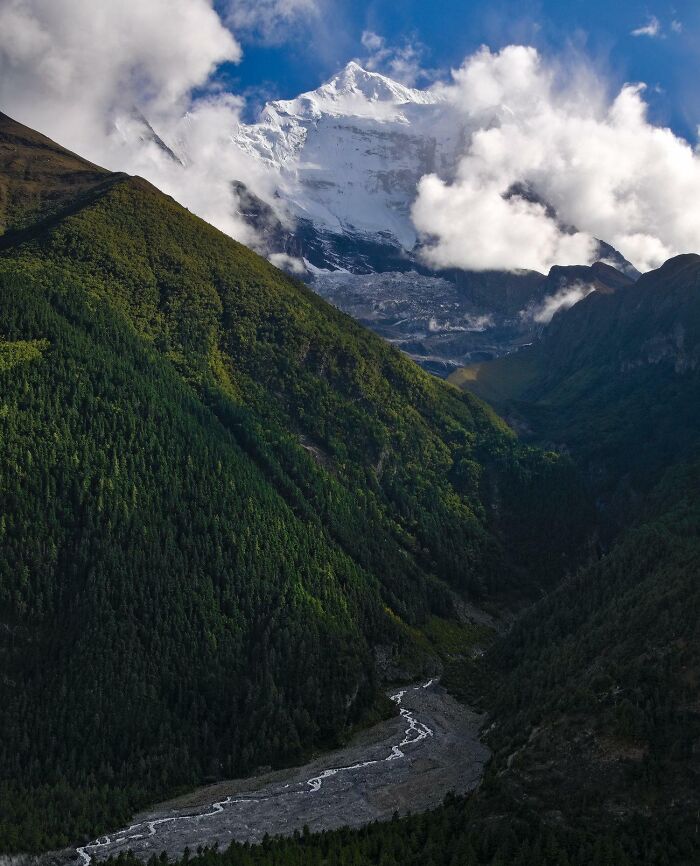Snow-covered famous landmark mountain towering above green forested valley with river from unexpected angles view