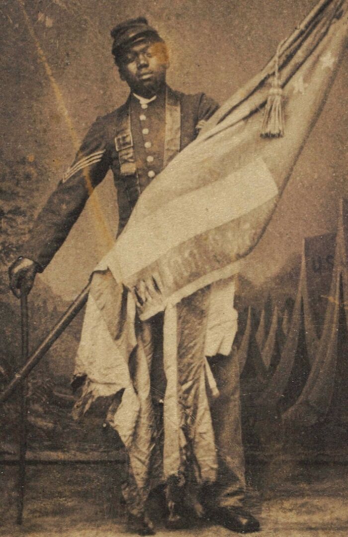 African American soldier in historic military uniform holding a flag, representing African American military history.