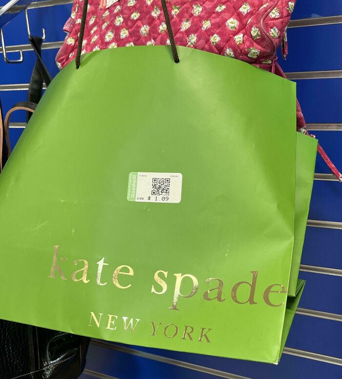 Green kate spade shopping bag with thrift store price tag hanging on a metal display rack with other bags behind it.