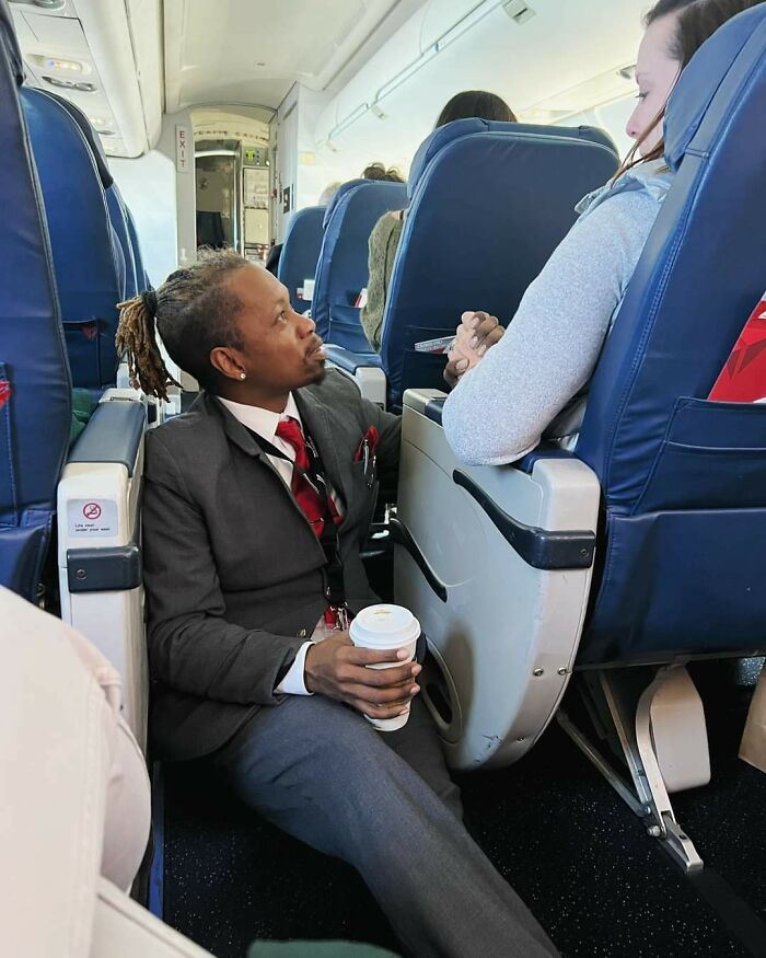 Flight attendant in uniform sitting on the plane floor comforting a passenger facing fear of flying during flight.
