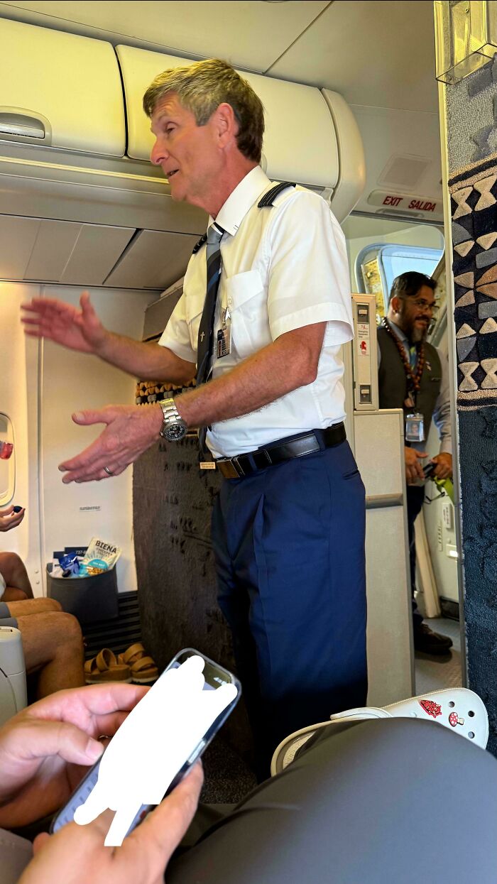 Pilot reassuring passengers inside airplane cabin, supporting those with fear of flying during flight preparation.