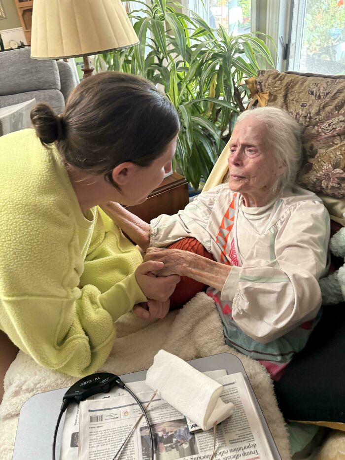 Young woman comforting elderly woman indoors, representing inspiring moments of overcoming fear of flying and travel challenges.