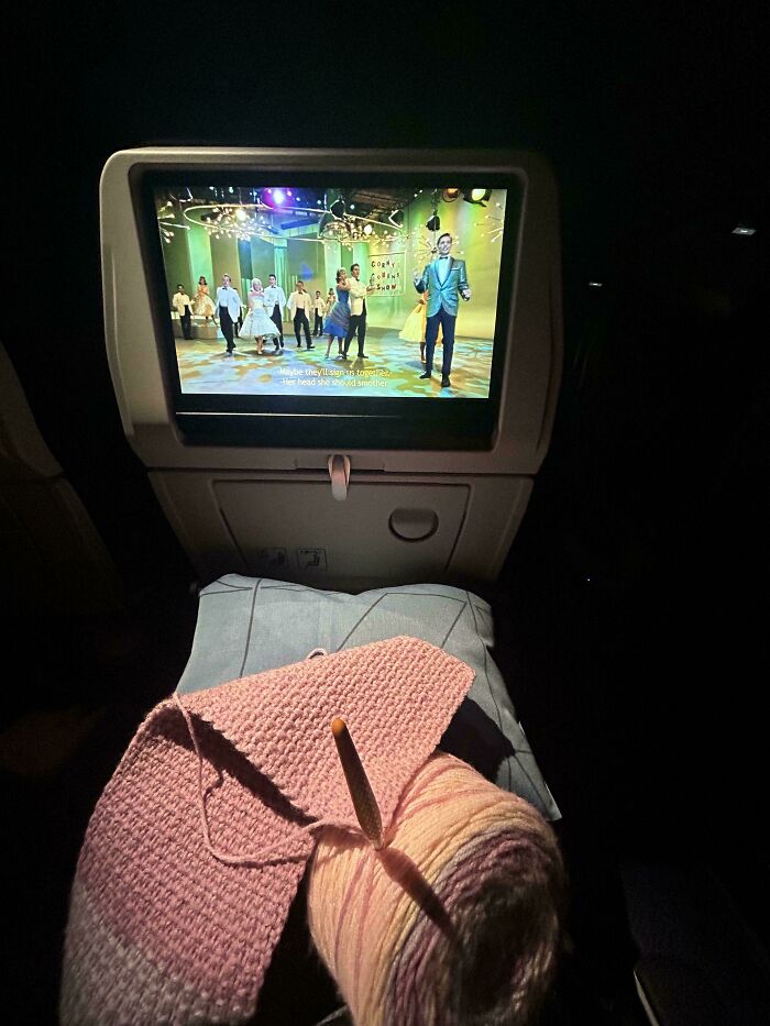 Knitting project and movie on airplane screen during a flight, showing people overcoming fear of flying.