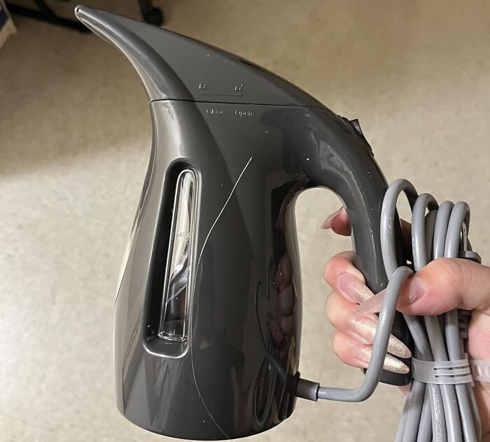 Hand holding a black handheld fabric steamer with cord, part of early Prime Day deals showing up before the event.