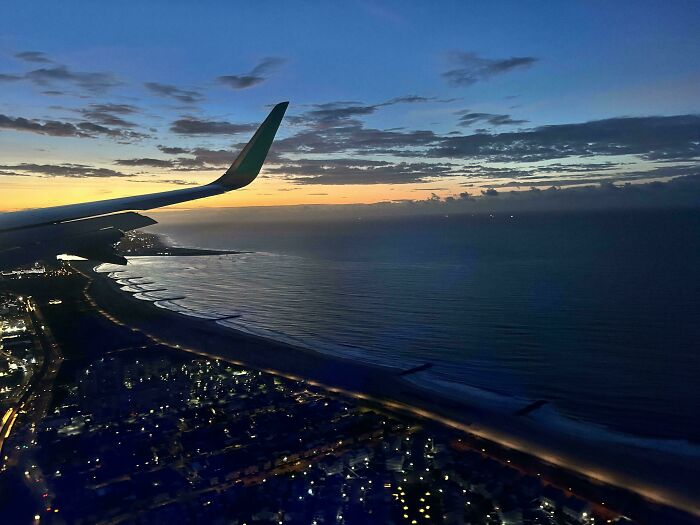 View from airplane window at dusk showing wing, coastline, and city lights, inspiring those overcoming fear of flying.