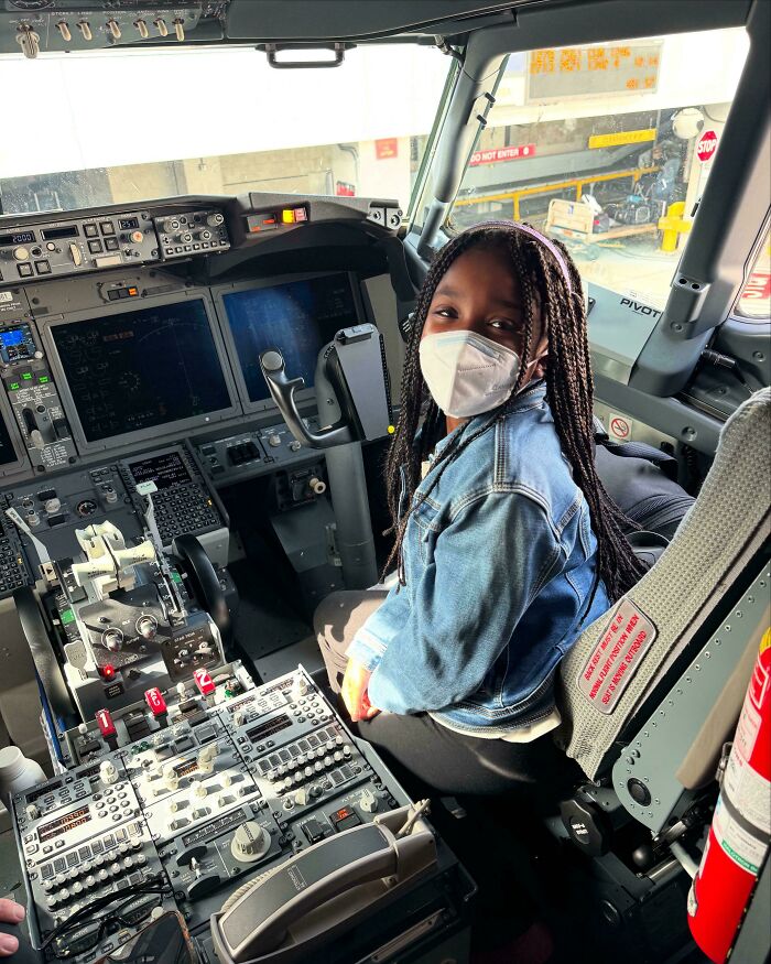 Young girl wearing a mask sitting in an airplane cockpit, showing inspiring courage to overcome fear of flying.