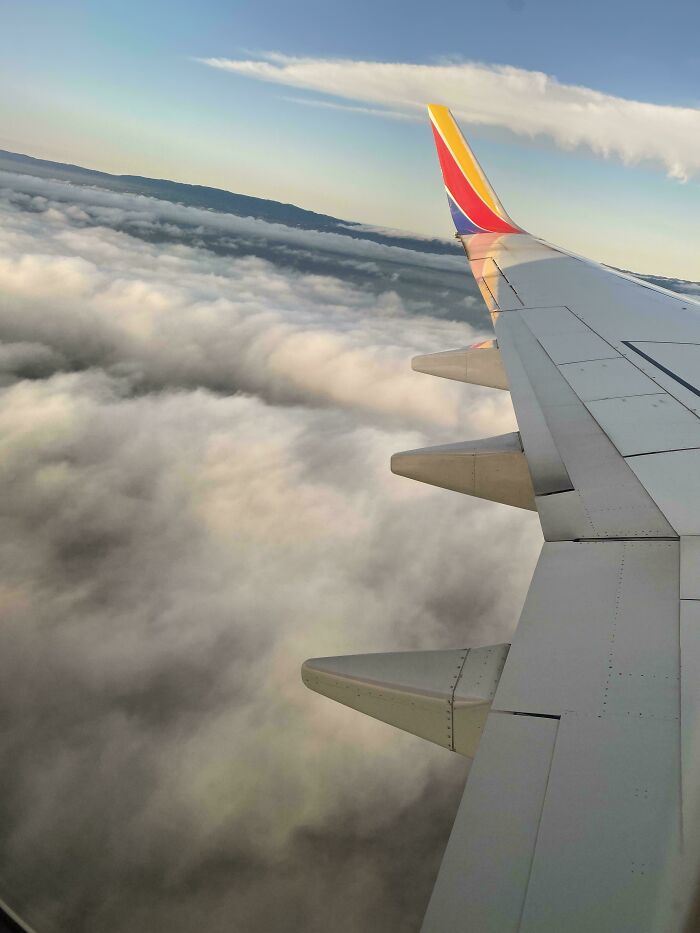 Airplane wing above the clouds during sunrise, inspiring moments of overcoming fear of flying and taking flight.