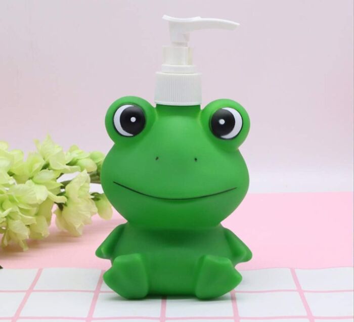 Green frog-shaped quirky gem soap dispenser sitting on a tiled surface with light flowers in the background.