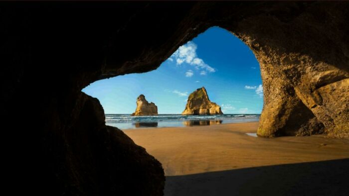 Vista desde el interior de una cueva hacia la playa con formaciones rocosas y cielo azul claro, terribles mentirosos.
