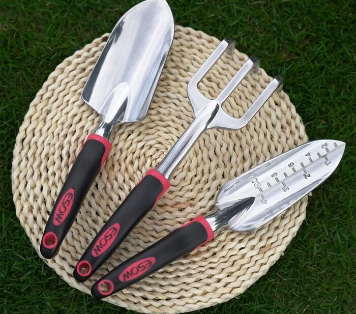 Set of three gardening tools with black and red handles on a woven mat, showcasing essential gardening tools for an outdoor oasis.