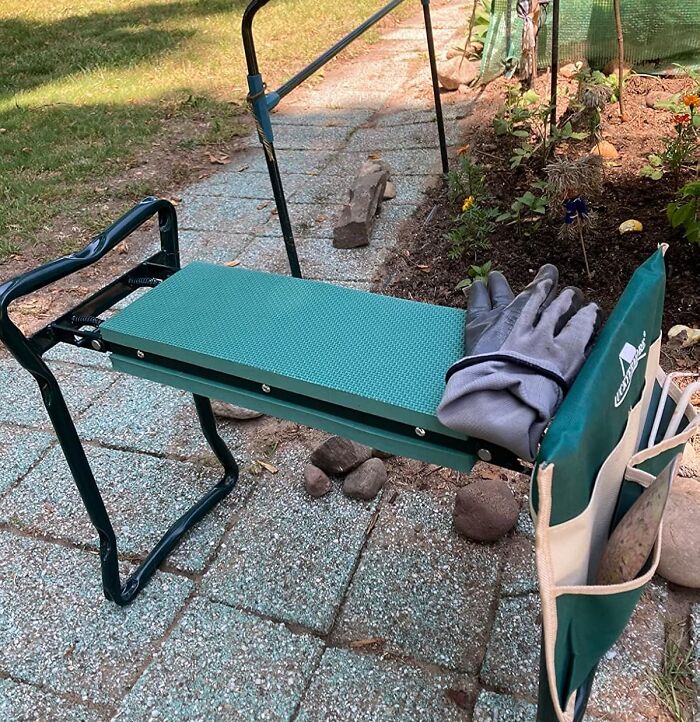 Gardening kneeler bench with gloves and tool pouch beside a garden bed, showcasing essential gardening tools and decor items.